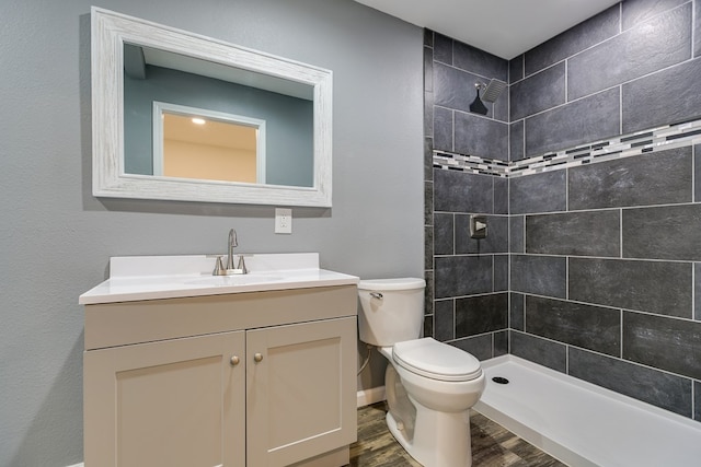 bathroom featuring tiled shower, wood-type flooring, toilet, and vanity