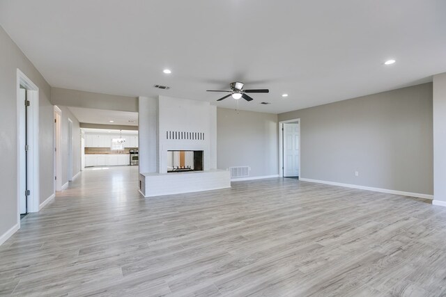 unfurnished living room featuring a multi sided fireplace, ceiling fan with notable chandelier, and light wood-type flooring