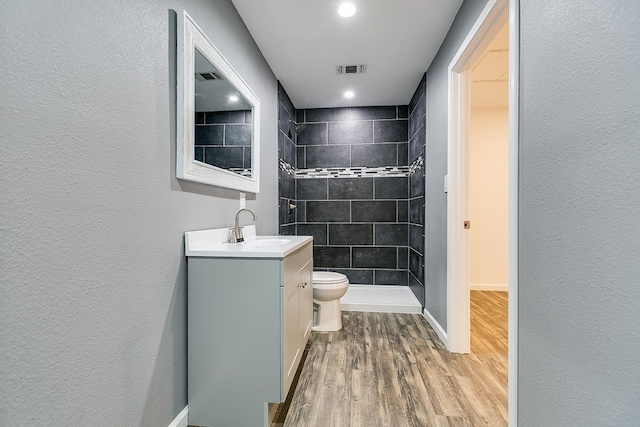 bathroom with hardwood / wood-style flooring, vanity, toilet, and a tile shower