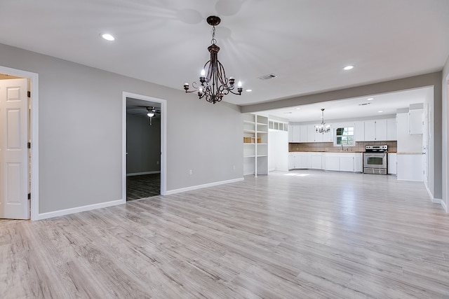 unfurnished living room with ceiling fan with notable chandelier and light hardwood / wood-style floors