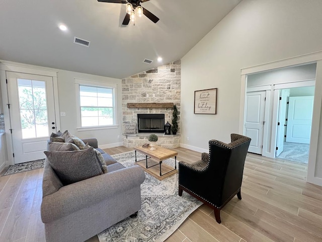 living room featuring vaulted ceiling, a stone fireplace, ceiling fan, and light hardwood / wood-style floors