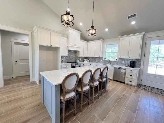 kitchen with stainless steel appliances, a center island, light stone counters, white cabinets, and decorative light fixtures