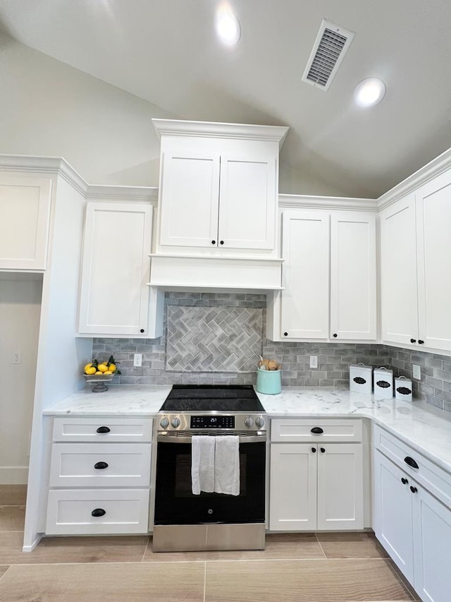 kitchen featuring vaulted ceiling, white cabinetry, decorative backsplash, stainless steel range with electric stovetop, and light stone counters