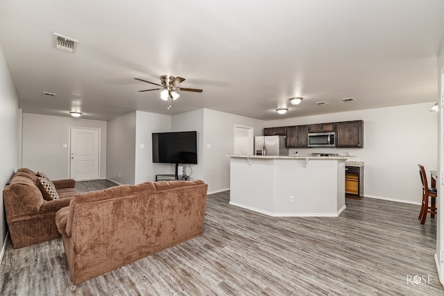 living room with baseboards, wood finished floors, visible vents, and a ceiling fan