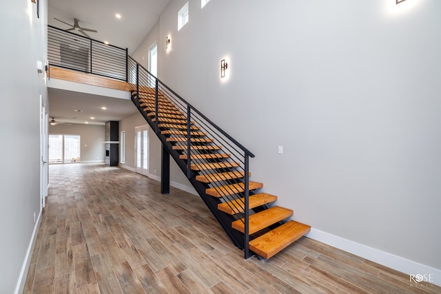 staircase with wood-type flooring, ceiling fan, and a high ceiling