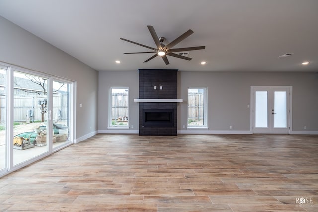 unfurnished living room with ceiling fan, a healthy amount of sunlight, a fireplace, and light wood-type flooring