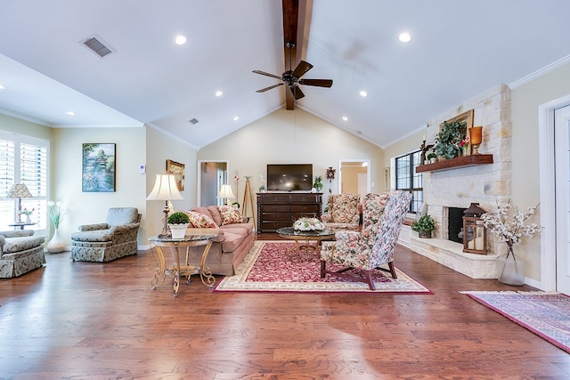living area with ceiling fan, visible vents, a stone fireplace, vaulted ceiling with beams, and wood finished floors