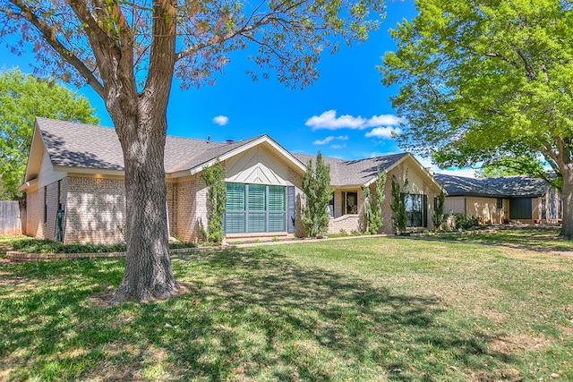 single story home featuring brick siding, a shingled roof, and a front yard