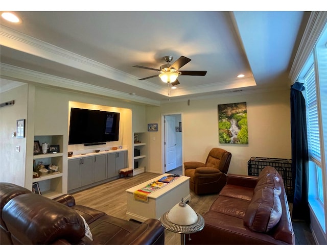 living room with light wood finished floors, a ceiling fan, ornamental molding, a tray ceiling, and recessed lighting