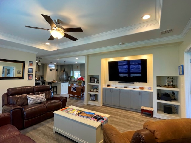 living area featuring a ceiling fan, visible vents, light wood-style floors, a raised ceiling, and crown molding