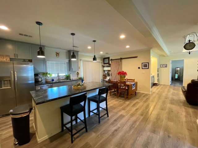 kitchen with a barn door, a sink, light wood-style floors, appliances with stainless steel finishes, and dark countertops