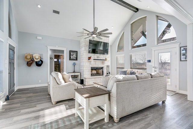 living room featuring beam ceiling, a stone fireplace, wood-type flooring, and high vaulted ceiling