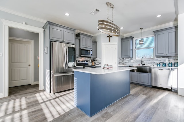 kitchen with sink, decorative light fixtures, ornamental molding, appliances with stainless steel finishes, and a kitchen island