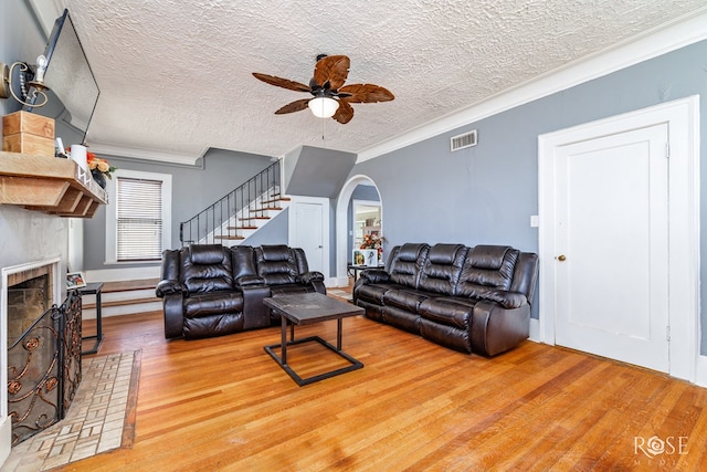 living room featuring a fireplace, wood-type flooring, ornamental molding, ceiling fan, and a textured ceiling