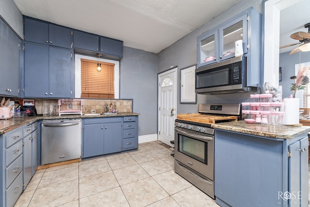 kitchen with blue cabinetry, a textured ceiling, light tile patterned floors, appliances with stainless steel finishes, and backsplash