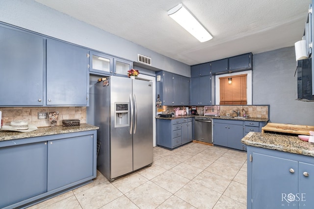 kitchen featuring blue cabinets, sink, stone countertops, a textured ceiling, and appliances with stainless steel finishes