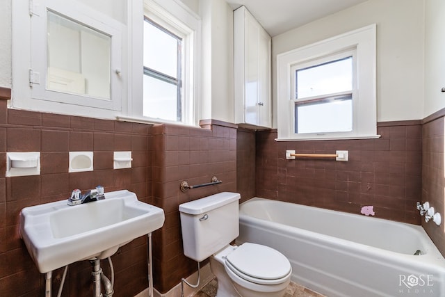 bathroom with a tub, plenty of natural light, tile walls, and toilet