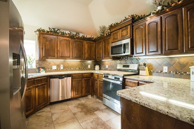 kitchen with light stone counters, tasteful backsplash, stainless steel appliances, and lofted ceiling