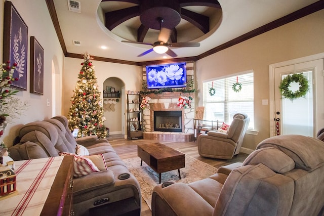 living room featuring crown molding, light hardwood / wood-style flooring, ceiling fan, a tray ceiling, and a fireplace