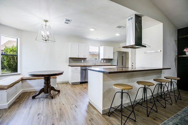 1106 Gregory Dr, San Angelo, TX 76905 - kitchen with island range hood, stainless steel appliances, dark countertops, a kitchen bar, and light wood-style floors