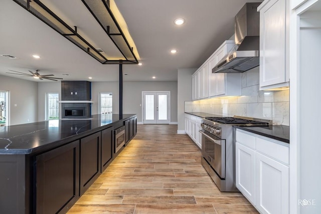 kitchen featuring a ceiling fan, open floor plan, stainless steel appliances, wall chimney range hood, and decorative backsplash