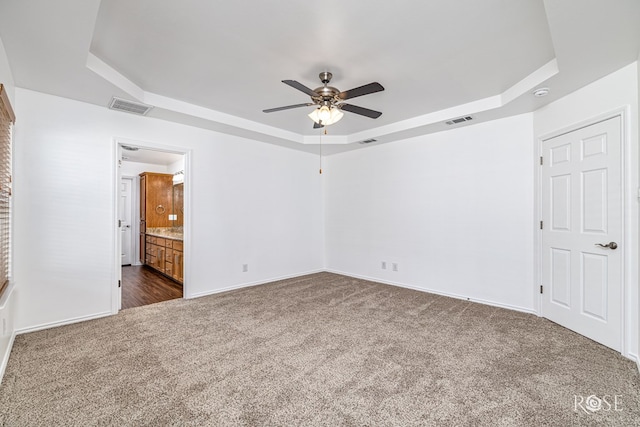 4129 Sedona Trl, San Angelo, TX 76904 - unfurnished bedroom with a tray ceiling, dark colored carpet, baseboards, ceiling fan, and ensuite bathroom