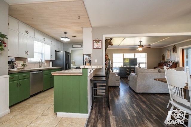 kitchen with appliances with stainless steel finishes, white cabinetry, a kitchen bar, green cabinetry, and plenty of natural light