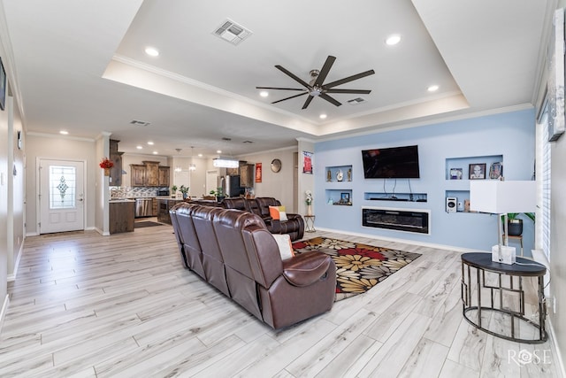 living room featuring a tray ceiling, ornamental molding, and light wood-type flooring