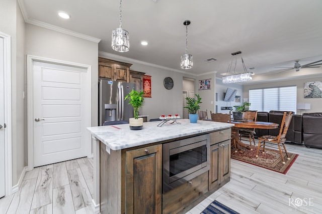 kitchen featuring decorative light fixtures, ornamental molding, stainless steel appliances, and a kitchen island