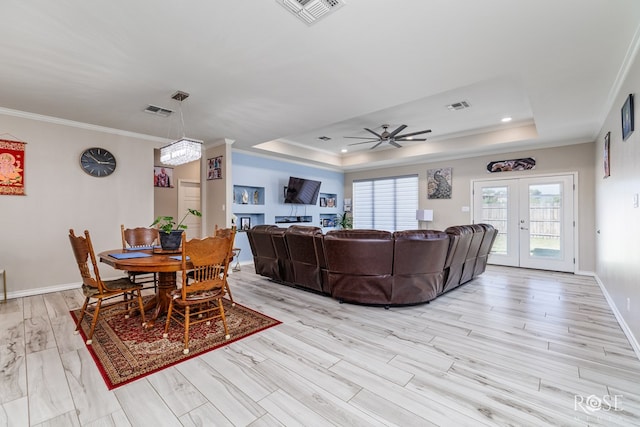 dining area featuring french doors, ornamental molding, a tray ceiling, and light wood-type flooring