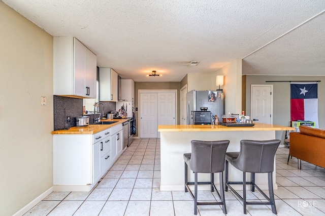 705 Fay St, Sonora, TX 76950 - kitchen with butcher block countertops, stainless steel appliances, a kitchen bar, white cabinets, and a textured ceiling