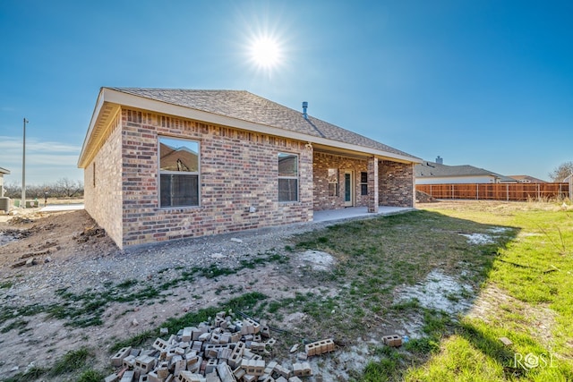 rear view of property with brick siding, a shingled roof, fence, a yard, and a patio area