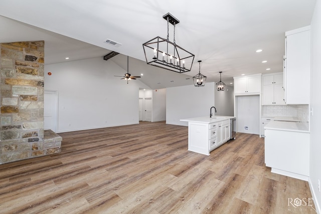 kitchen featuring a center island with sink, light countertops, visible vents, open floor plan, and white cabinetry