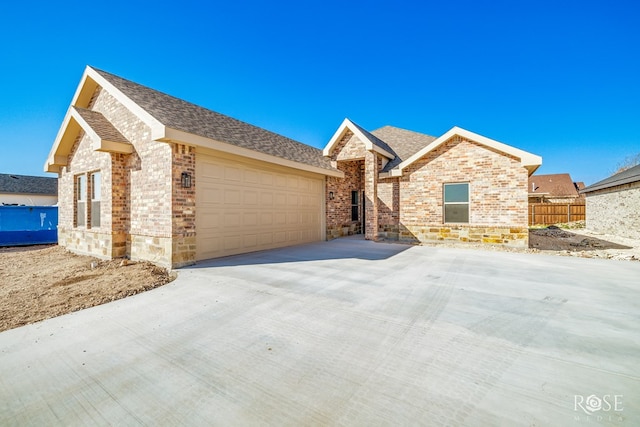 ranch-style home featuring a shingled roof, concrete driveway, brick siding, and an attached garage