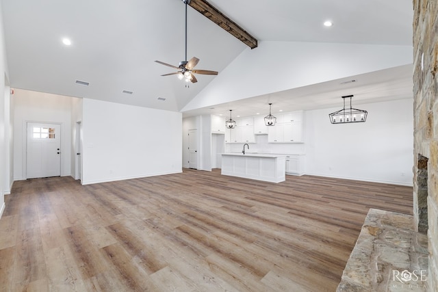 unfurnished living room with ceiling fan, high vaulted ceiling, light wood finished floors, and a sink