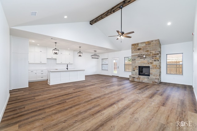 unfurnished living room featuring dark wood-style flooring, a ceiling fan, a stone fireplace, high vaulted ceiling, and beamed ceiling