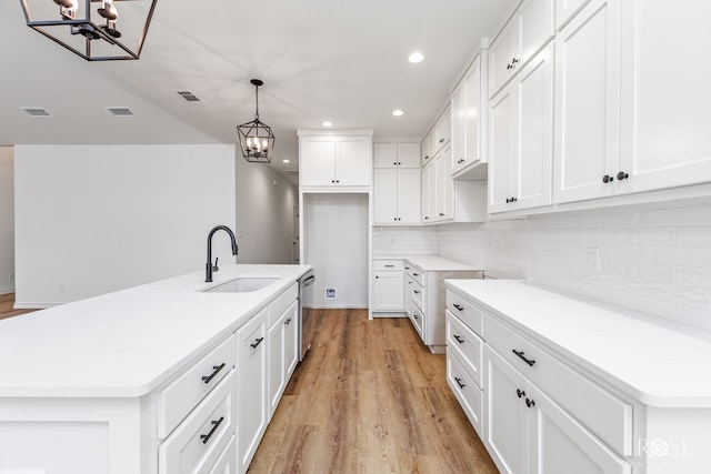 kitchen featuring light countertops, stainless steel dishwasher, white cabinetry, a sink, and an island with sink