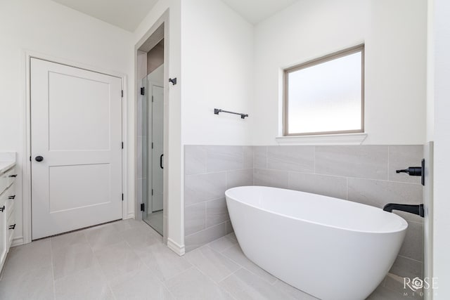 full bath with tile patterned floors, vanity, a freestanding tub, a shower stall, and tile walls