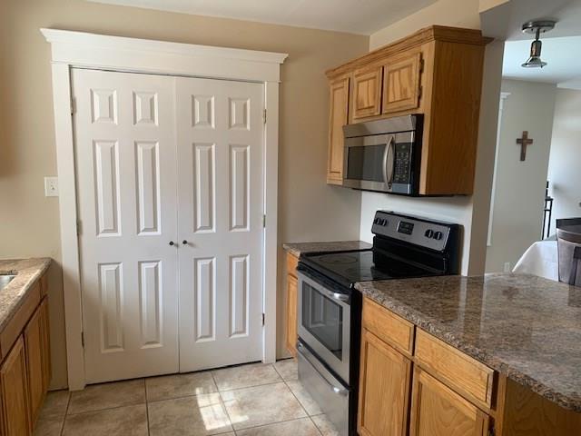 kitchen with dark stone countertops, light tile patterned floors, and appliances with stainless steel finishes