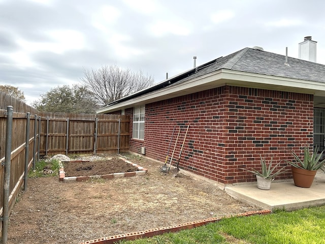 3570 Grandview Dr, San Angelo, TX 76904 - view of property exterior with a fenced backyard, brick siding, a vegetable garden, a chimney, and roof with shingles