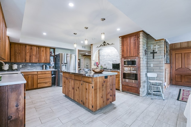 6290 Stokes Rd, San Angelo, TX 76904 - kitchen featuring appliances with stainless steel finishes, tasteful backsplash, a kitchen island, decorative light fixtures, and brown cabinets