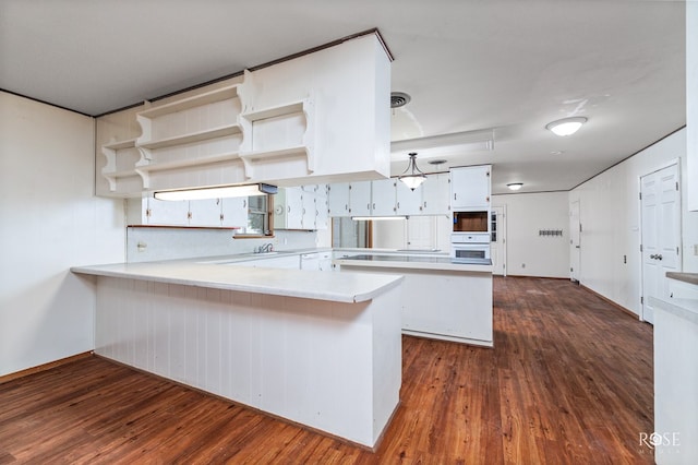 kitchen featuring white oven, dark wood-type flooring, white cabinets, and kitchen peninsula