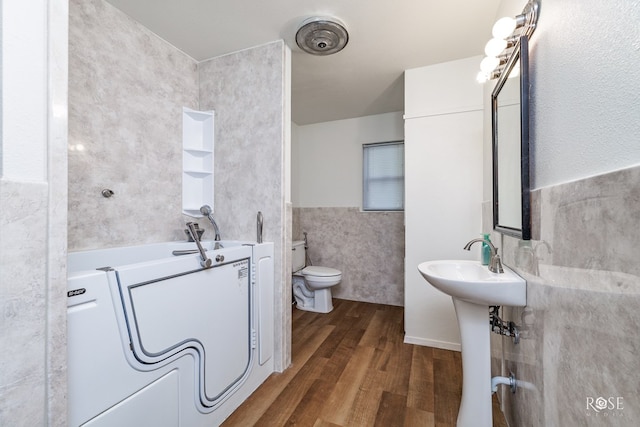 bathroom with sink, tile walls, hardwood / wood-style floors, a bath, and toilet