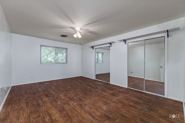 unfurnished bedroom with multiple closets, dark hardwood / wood-style floors, a barn door, and ceiling fan