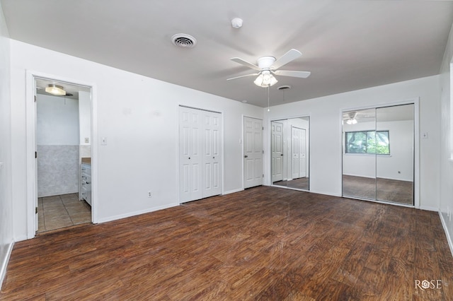 unfurnished bedroom featuring two closets, dark wood-type flooring, and ceiling fan