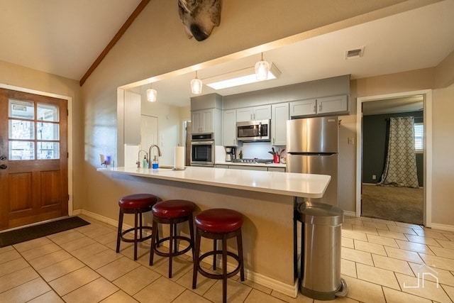 kitchen featuring pendant lighting, gray cabinets, a breakfast bar, appliances with stainless steel finishes, and kitchen peninsula