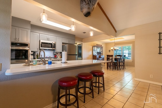 kitchen featuring light tile patterned floors, a breakfast bar area, gray cabinets, appliances with stainless steel finishes, and vaulted ceiling