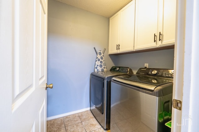 laundry area featuring washer and clothes dryer, a textured ceiling, cabinet space, light tile patterned flooring, and baseboards