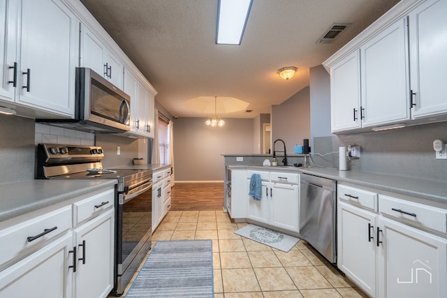 kitchen featuring visible vents, light tile patterned floors, decorative backsplash, white cabinets, and stainless steel appliances