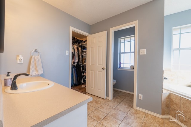 full bathroom featuring a walk in closet, toilet, tile patterned flooring, a bath, and vanity